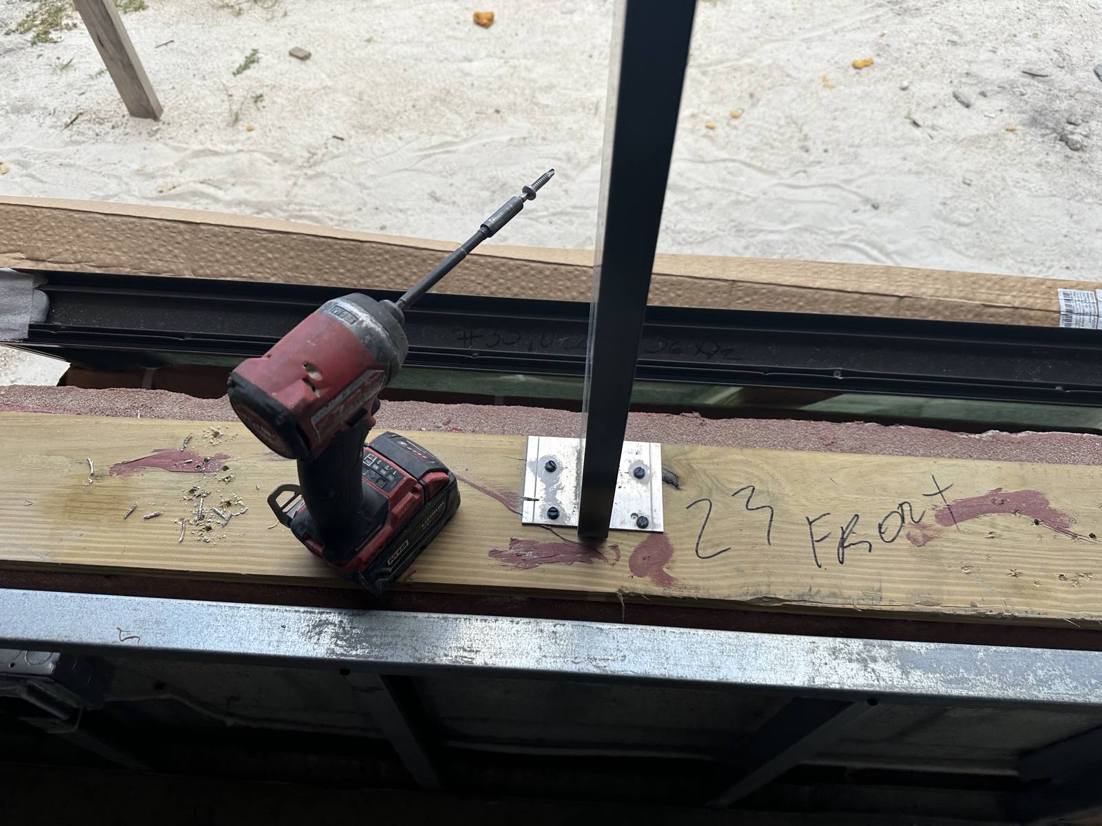 Black mullion secured with an anchor clip to the sill buck, impact driver beside it