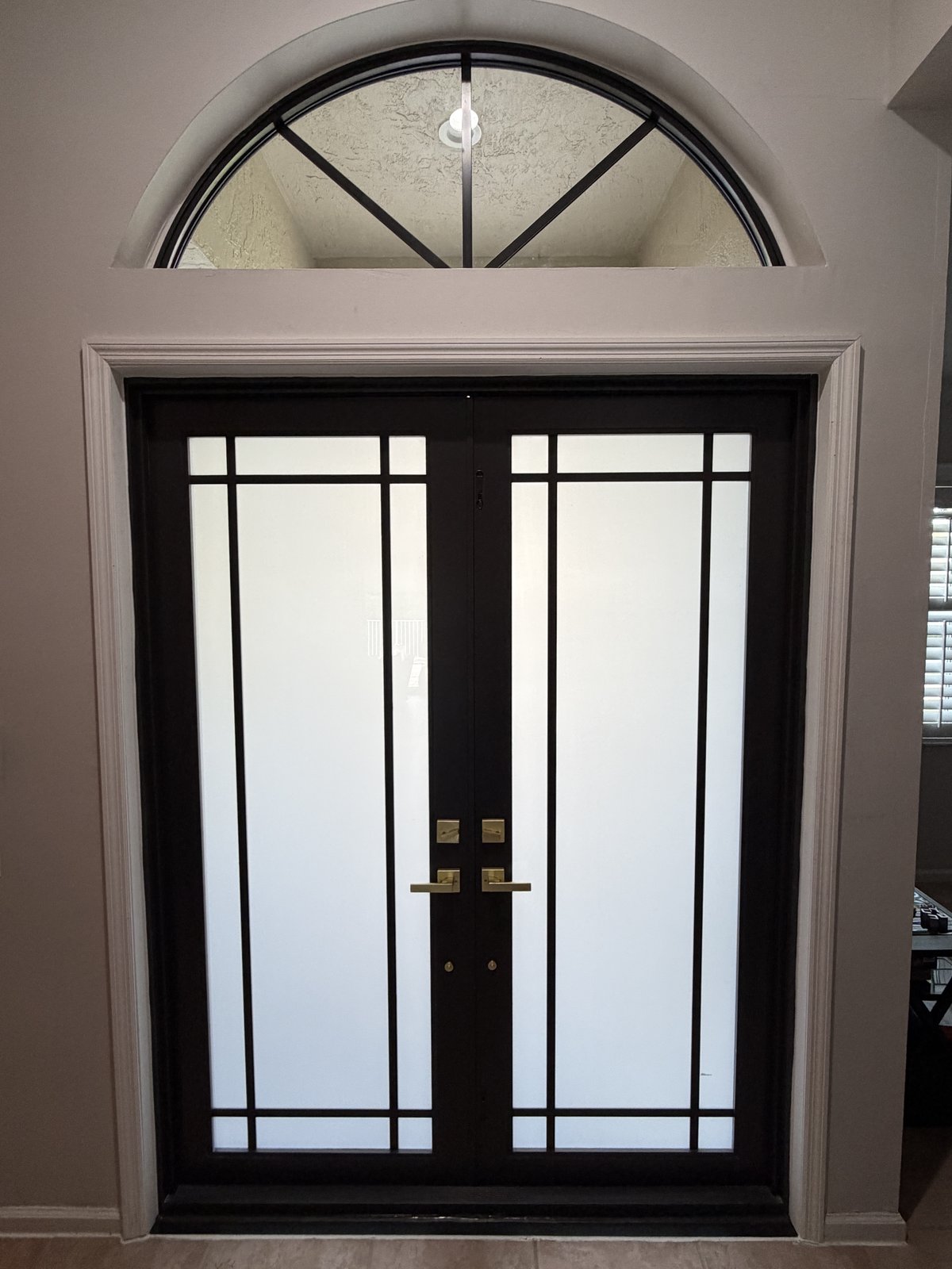 Black French doors with frosted glass and grids under an arched transom